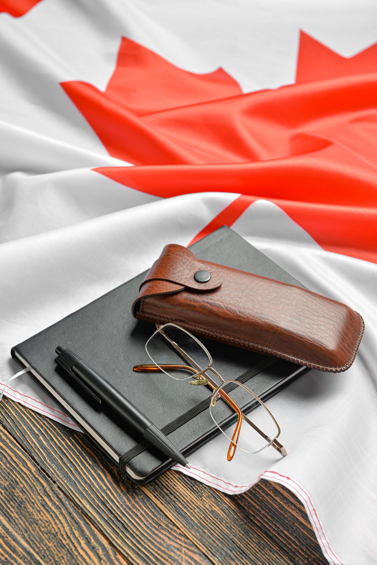 Notebook with Pen, Eyeglasses and Canadian Flag on Dark Wooden Background